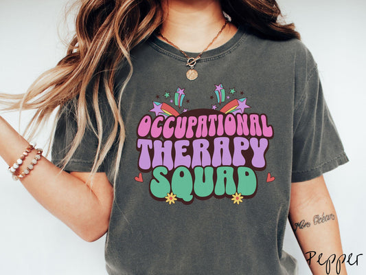 A vintage, pepper colored Comfort Colors T-shirt with the text Occupational Therapy Squad in colorful font with red hearts, sunflowers, and shooting stars mixed in.