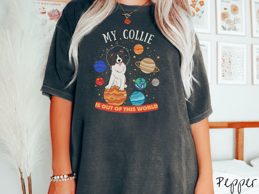 A vintage Comfort Colors t-shirt featuring the text My Collie is Out of This World. The design showcases an adorable Border Collie sitting proudly atop Jupiter, surrounded by a vibrant solar system filled with colorful planets and twinkling stars.