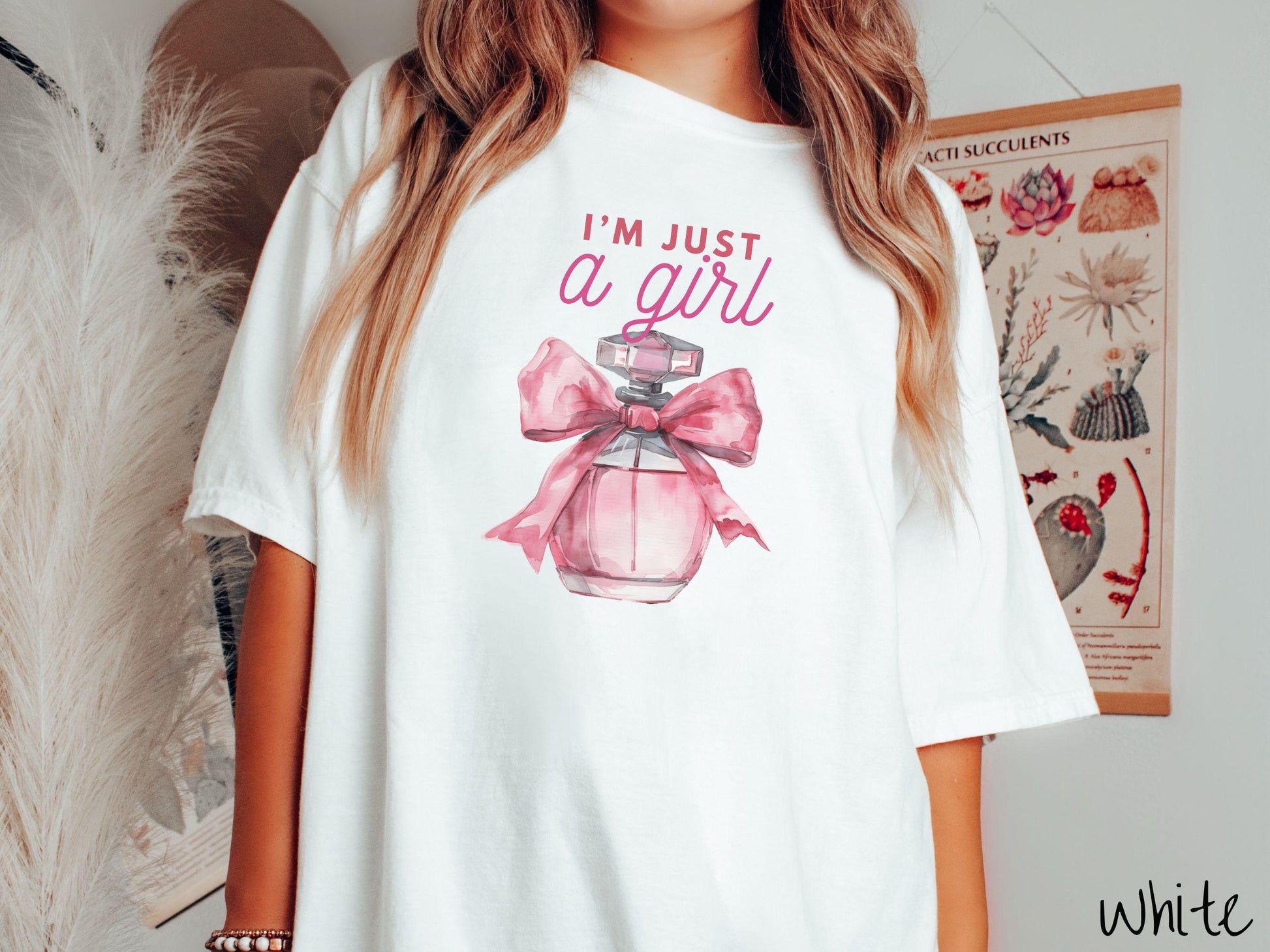 A stylish Comfort Colors T-shirt featuring the phrase &quot;I&#39;m Just a Girl&quot; in pink font above a bottle of pink perfume tied with a pink bow. This tee exudes a feminine and trendy vibe, perfect for those who appreciate unique fashion statements.