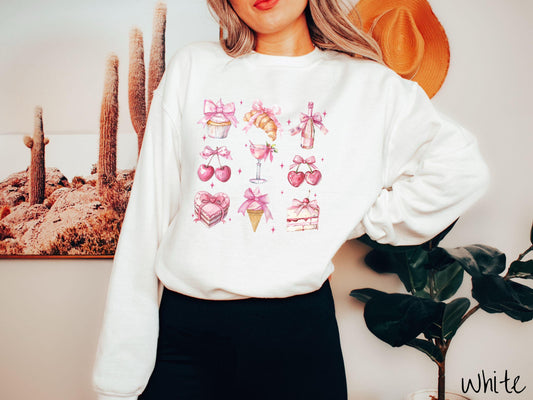 A stylish coquette Gildan sweatshirt featuring a grid of assorted treats with pink ribbons like a cupcake, a croissant, a champaigne bottle, cherries, a pink martini, a pink cake, and a pink ince cream cone, along with twinkling pink stars.