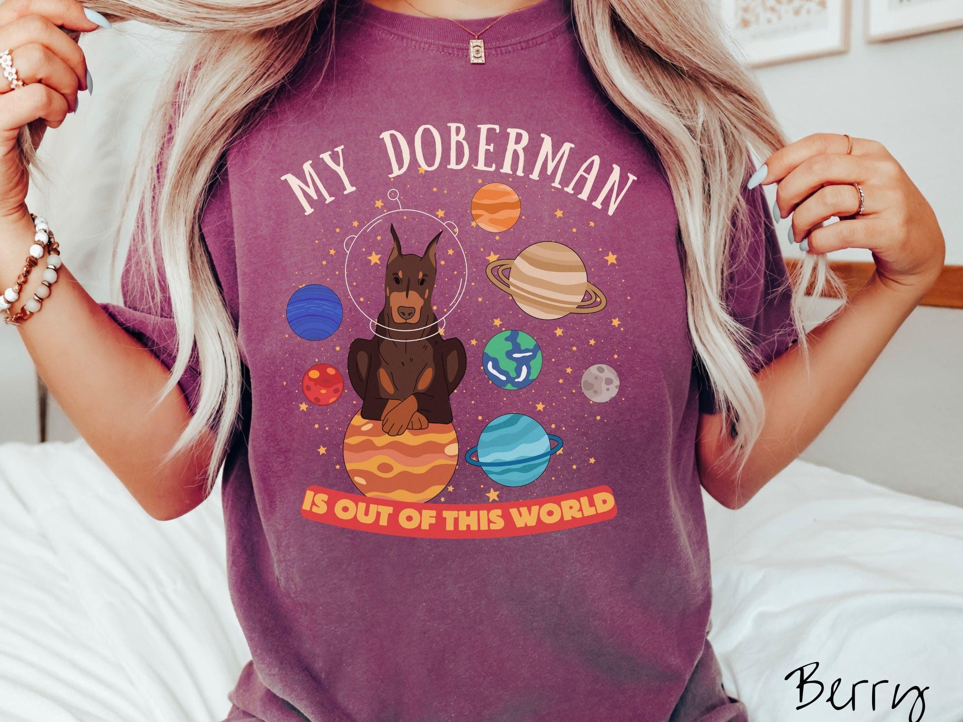 A vintage Comfort Colors t-shirt featuring the text My Doberman is Out of This World. The design showcases a Doberman sitting proudly atop Jupiter, surrounded by a vibrant solar system filled with colorful planets and twinkling stars.