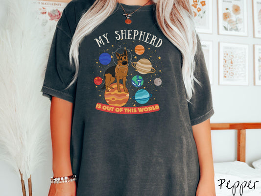 A vintage Comfort Colors t-shirt featuring the text My Shepherd is Out of This World. The design showcases a German Shepherd sitting proudly atop Jupiter, surrounded by a vibrant solar system filled with colorful planets and twinkling stars.