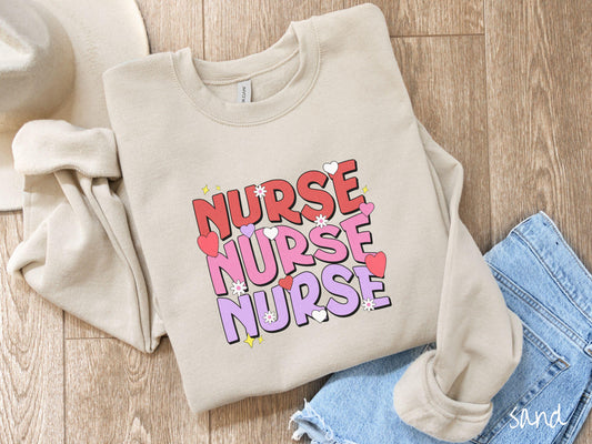 A stylish Gildan Sweatshirt featuring the word &quot;NURSE&quot; written three times vertically in red, pink, and purple font. There are red, white, and purple hearts mixed into the design as well as yellow twinkling stars.