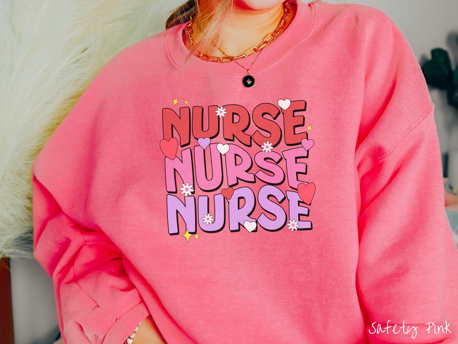 A stylish Gildan Sweatshirt featuring the word &quot;NURSE&quot; written three times vertically in red, pink, and purple font. There are red, white, and purple hearts mixed into the design as well as yellow twinkling stars.