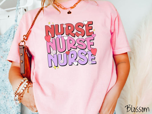 A stylish Comfort Colors T-shirt featuring the word &quot;NURSE&quot; written three times vertically in red, pink, and purple font. There are red, white, and purple hearts mixed into the design as well as yellow twinkling stars.