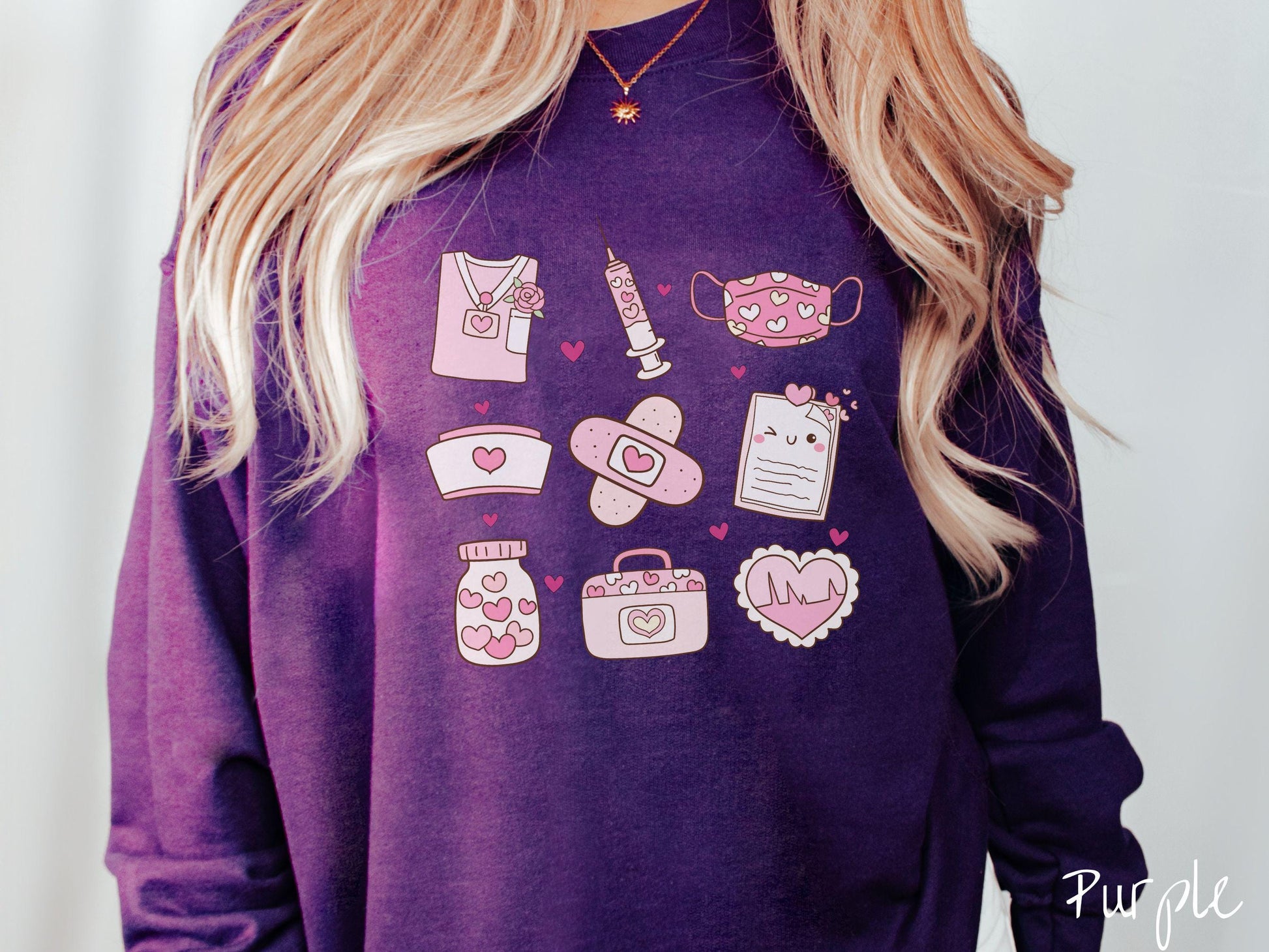 A Gildan sweatshirt featuring a 3x3 grid of nursing-themed illustrations adorned with heart designs like nursing scrubs, syringes, a face mask, a nurse cap, bandages, medical records, vitamins, a medical bag, and a heart-shaped EKG graph.