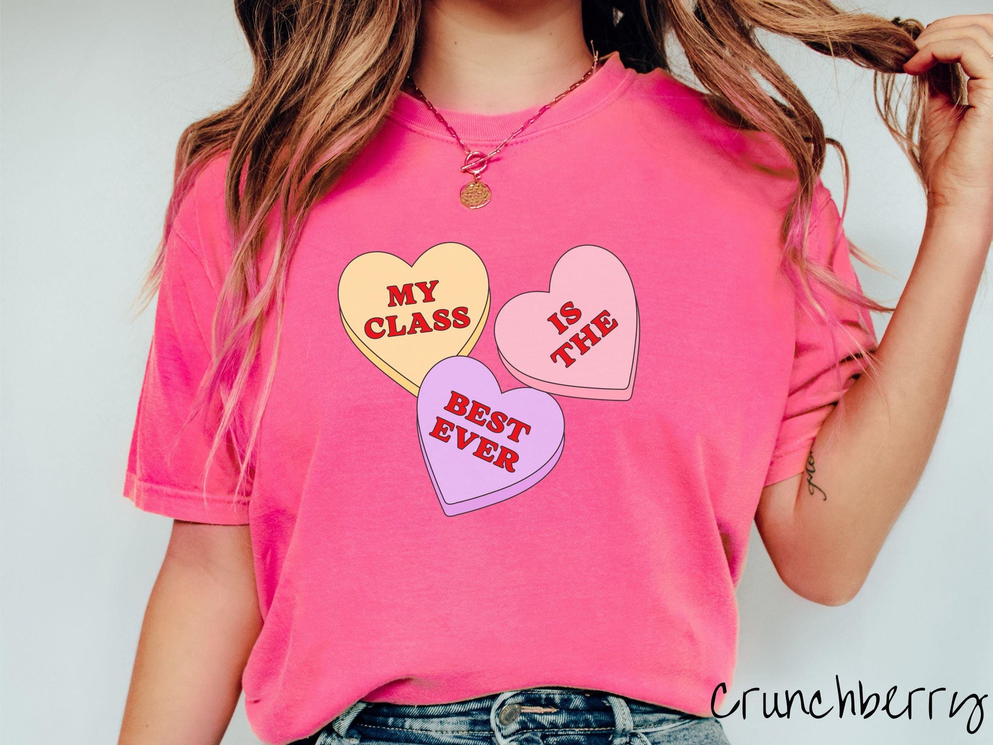 A charming vintage-style Valentine’s Day Comfort Colors t-shirt featuring three vibrant conversation hearts in yellow, red, and purple, this design displays the text “My class is the best ever” spread across the hearts.