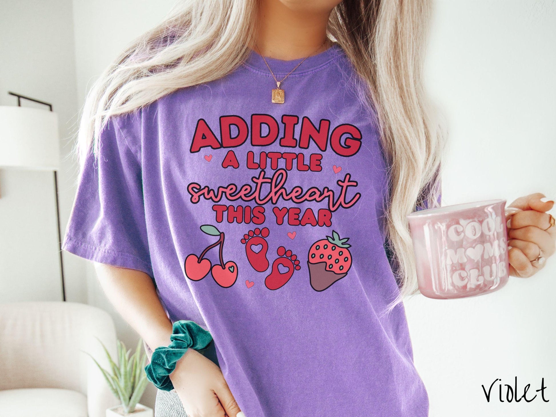 Share your exciting news with this vintage Comfort Colors t-shirt featuring the phrase “Adding a little sweetheart this year” in bold red font, paired with two red baby footprints framed by two red cherries and a chocolate-covered strawberry.