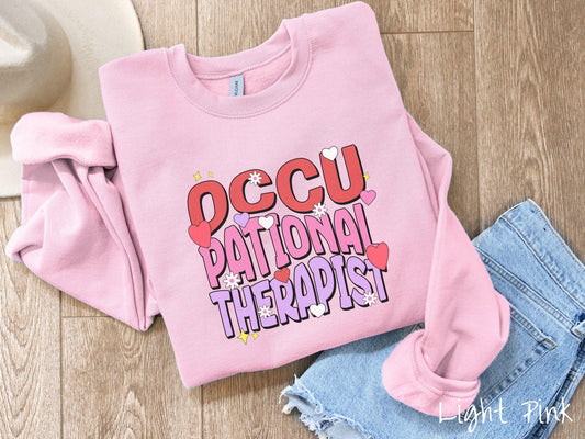 A stylish Gildan sweatshirt featuring the words &quot;Occupational Therapist&quot; arranged vertically in bold red, pink, and purple font, this design is enhanced with colorful hearts, flowers, and stars for a playful, uplifting touch.