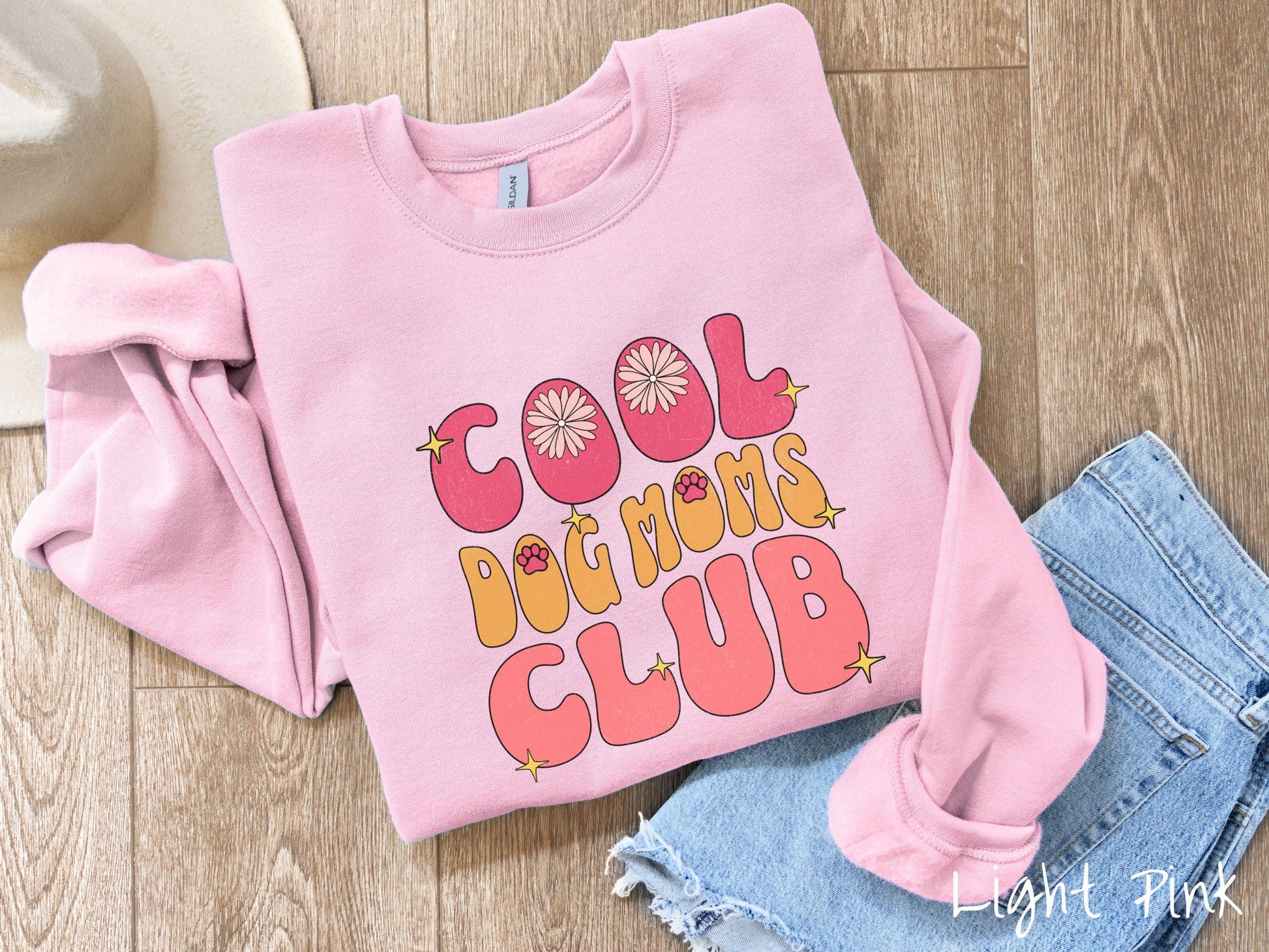 A vintage Gildan sweatshirt featuring the playful text Cool Dog Moms Club, this design is full of charming details. From flower petals nestled in the "O" of COOL to a cute red paw print in the "O" of DOG and sparkling yellow stars throughout.