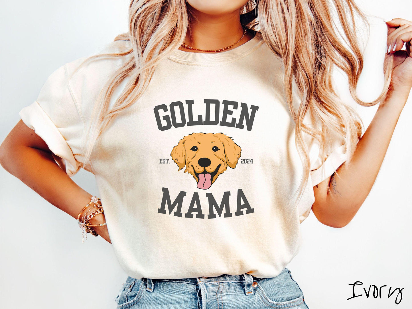 A vintage Comfort Colors t-shirt features a design with the words Golden Mama in a classic university-style font, framing an adorable black and orange Golden Retriever with its tongue out. The playful touch of EST. 2024 adds charm to the design.