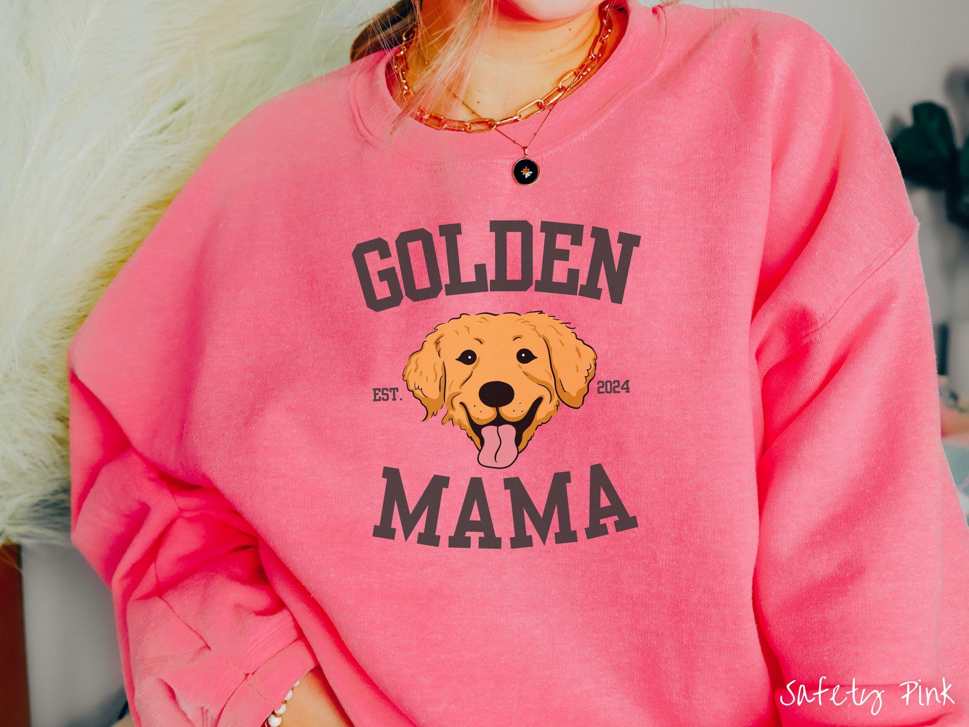A vintage Gildan sweatshirt features a design with the words Golden Mama in a classic university-style font, framing an adorable black and orange Golden Retriever with its tongue out. The playful touch of EST. 2024 adds charm to the design.