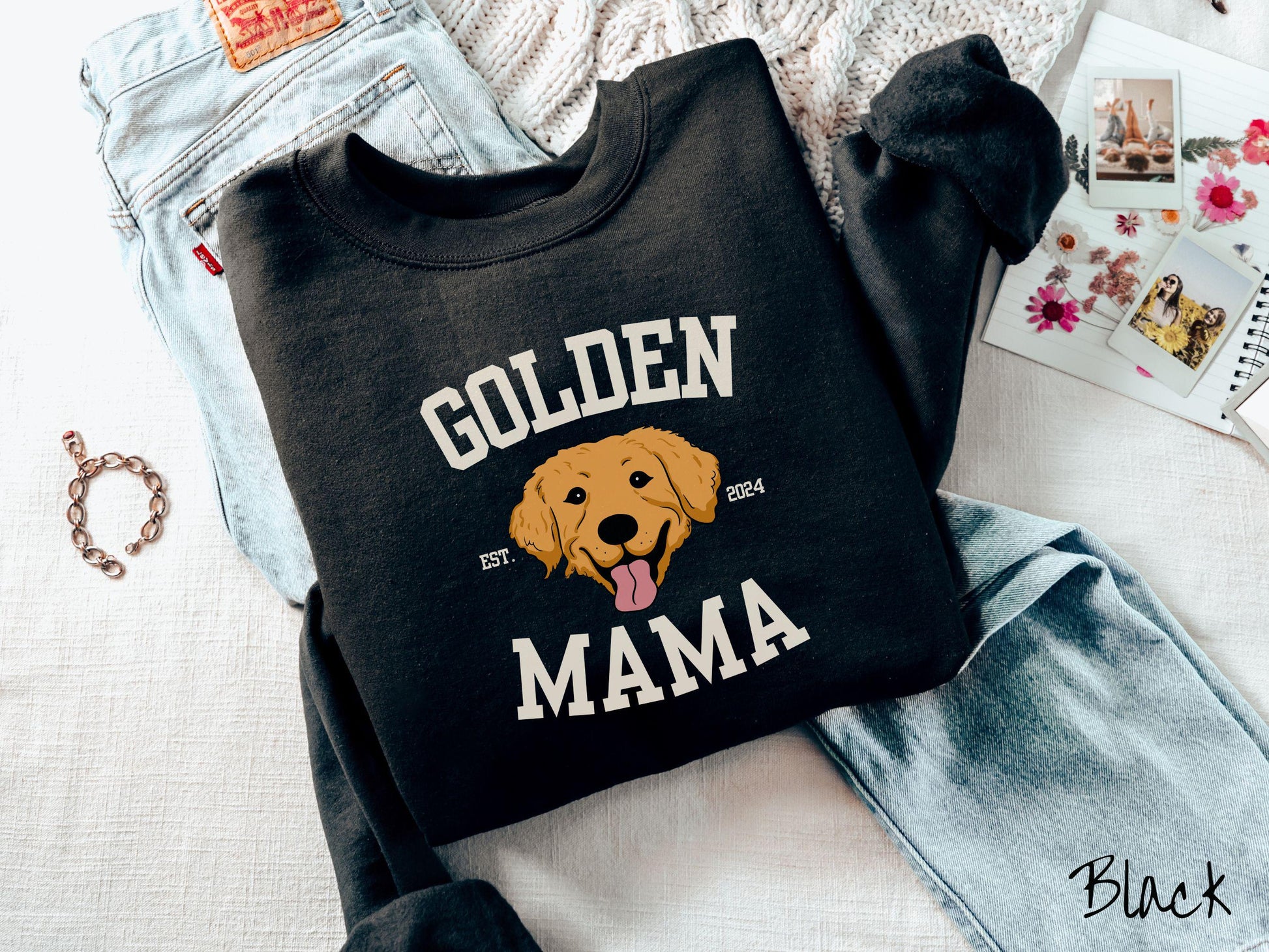 A vintage Gildan sweatshirt features a design with the words Golden Mama in a classic university-style font, framing an adorable black and orange Golden Retriever with its tongue out. The playful touch of EST. 2024 adds charm to the design.