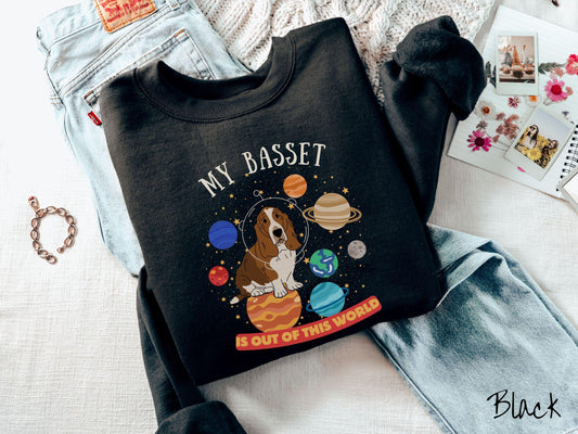 A vintage Gildan sweatshirt featuring the playful text &#39;My Basset is Out of This World&#39;. The design showcases a basset hound sitting proudly atop Jupiter, surrounded by a vibrant solar system filled with colorful planets and twinkling stars.