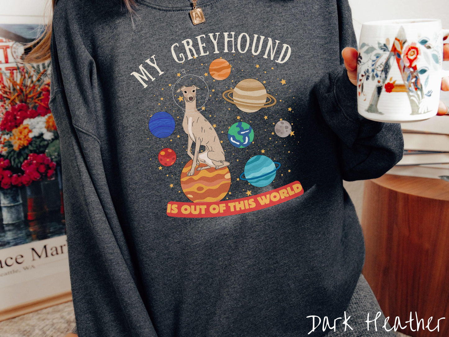 A vintage Gildan sweatshirt featuring the text My Greyhound is Out of This World. The design showcases a Greyhound sitting proudly atop Jupiter, surrounded by a vibrant solar system filled with colorful planets and twinkling stars.