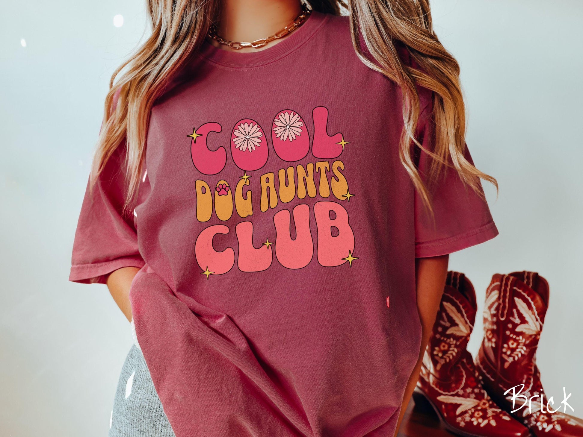 A vintage Comfort Colors t-shirt featuring the text "Cool Dog Aunts Club" in bold red, yellow, and orange fonts with flower petals nestled in the "O" of COOL, a cute red paw print in the "O" of DOG, and sparkling yellow stars throughout.