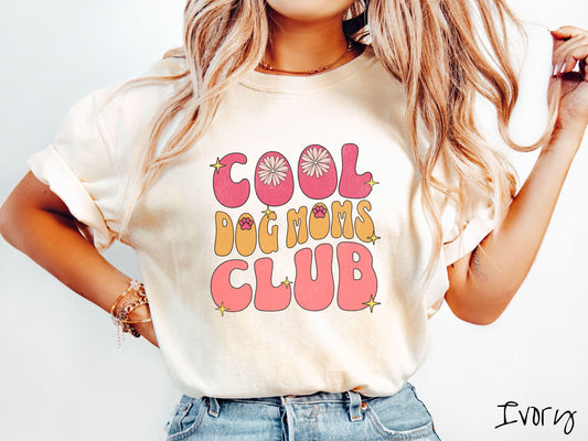 A vintage Comfort Colors t-shirt featuring the playful text Cool Dog Moms Club, this design is full of charming details. From flower petals nestled in the &quot;O&quot; of COOL to a cute red paw print in the &quot;O&quot; of DOG and sparkling yellow stars throughout.