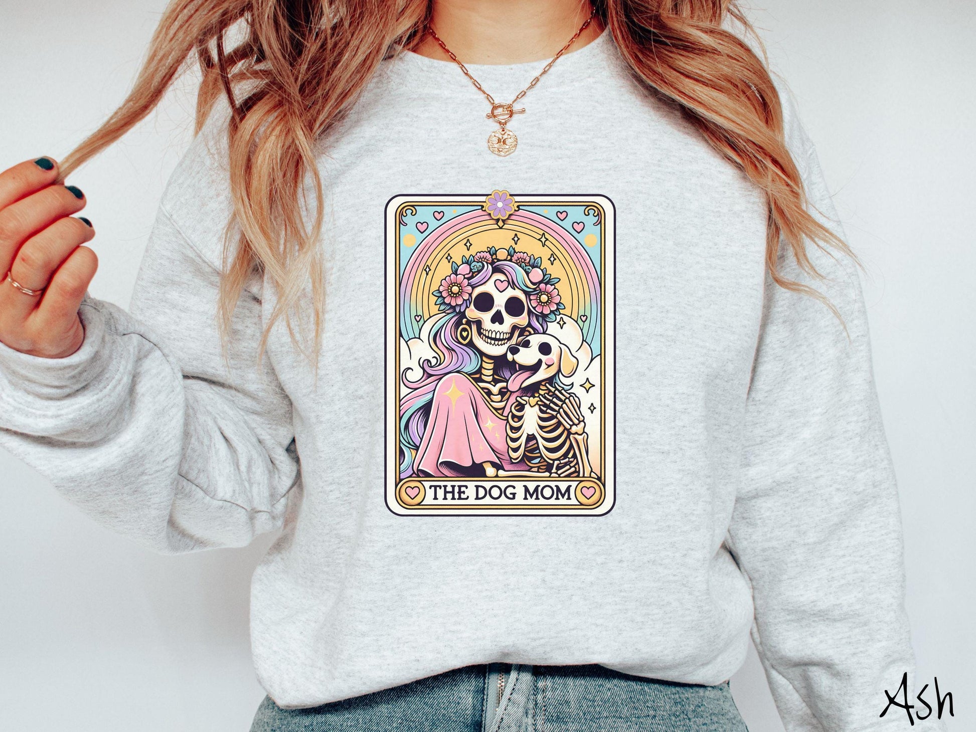 A vintage Gildan sweatshirt features a tarot card design with the text “The Dog Mom” along the bottom, framed by red hearts. Inside the tarot card is a female skeleton with flowing hair adorned with colorful flowers holding a skeleton dog.