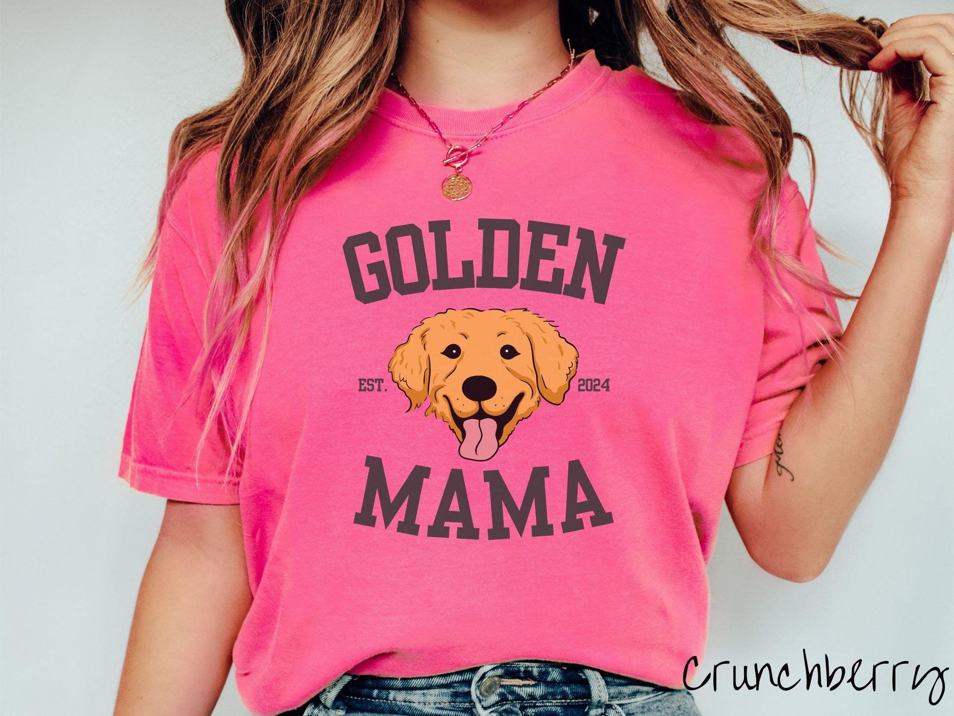 A vintage Comfort Colors t-shirt features a design with the words Golden Mama in a classic university-style font, framing an adorable black and orange Golden Retriever with its tongue out. The playful touch of EST. 2024 adds charm to the design.