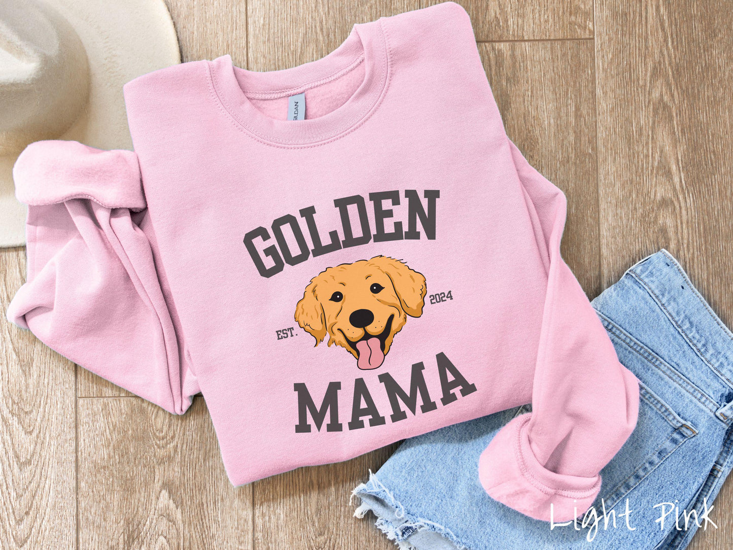 A vintage Gildan sweatshirt features a design with the words Golden Mama in a classic university-style font, framing an adorable black and orange Golden Retriever with its tongue out. The playful touch of EST. 2024 adds charm to the design.