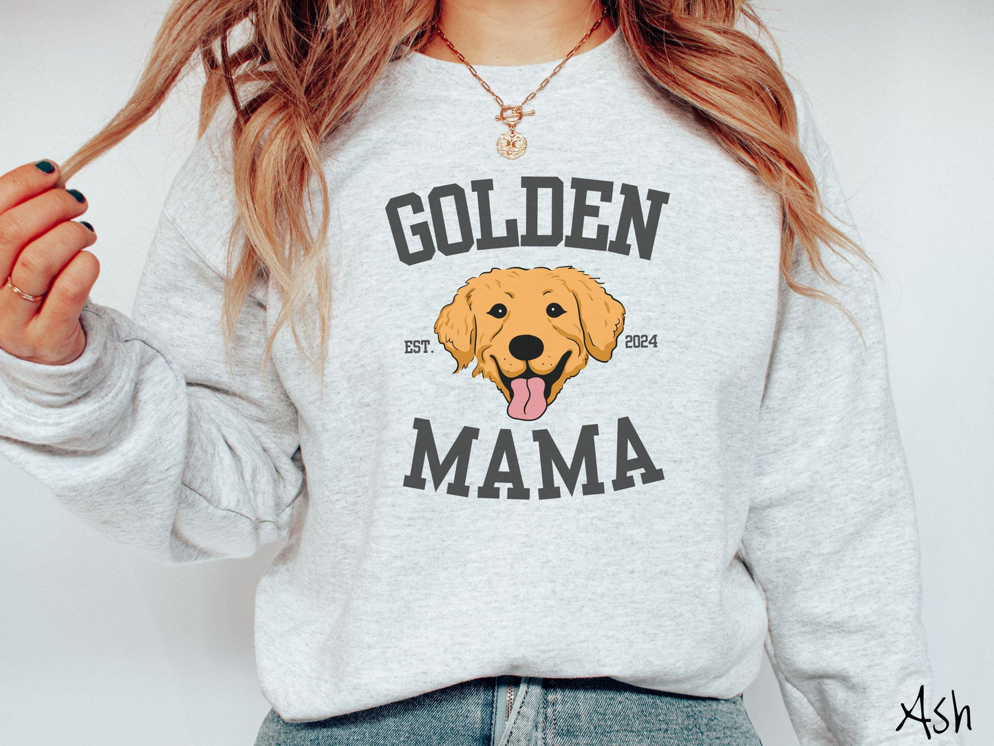 A vintage Gildan sweatshirt features a design with the words Golden Mama in a classic university-style font, framing an adorable black and orange Golden Retriever with its tongue out. The playful touch of EST. 2024 adds charm to the design.