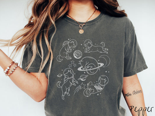 A vintage Comfort Colors t-shirt perfect for dog lovers and space enthusiasts alike, featuring outline designs of dogs in astronaut bubble helmets. This design showcases pups floating in the solar system, surrounded by stars, the moon, and planets.
