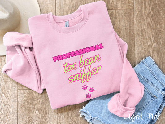 A vintage Gildan sweatshirt perfect for dog lovers who can’t resist those adorable toe beans! It features the funny text Professional Toe Bean Sniffer in bold pink and green fluorescent font, and below the text are three pink dog paw prints.
